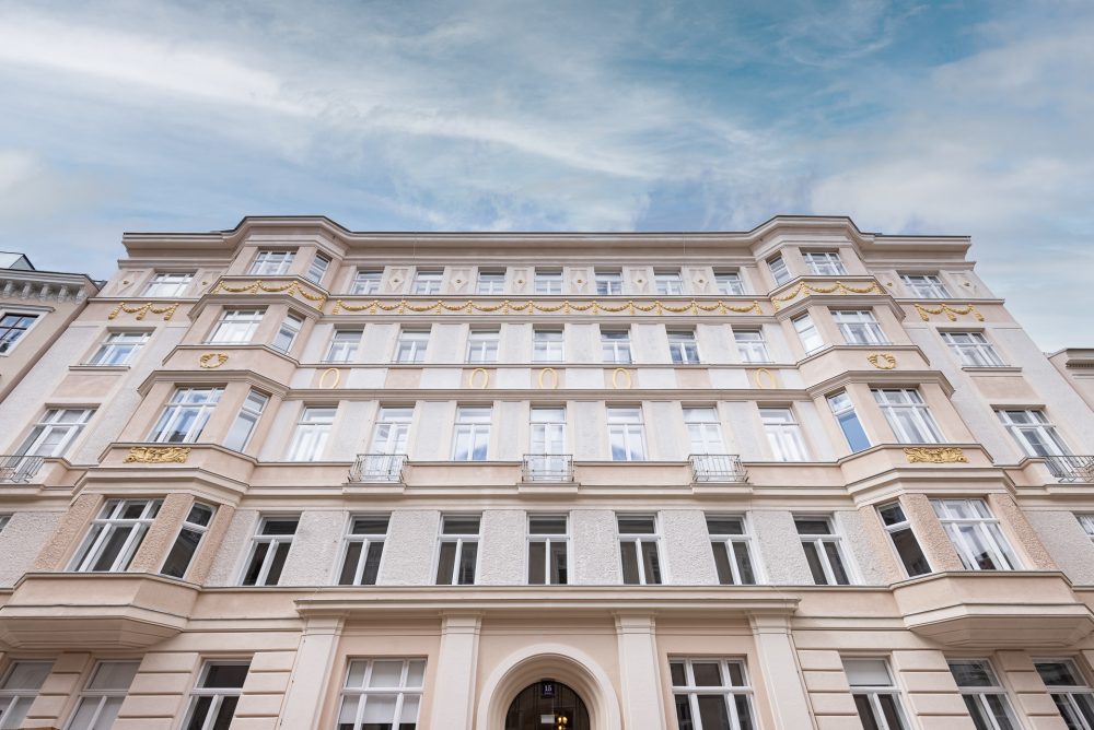 Vorderansicht eines mehrstöckigen, eleganten Altbaus mit verzierten Fassadenelementen und symmetrisch angeordneten, weißen Fenstern.