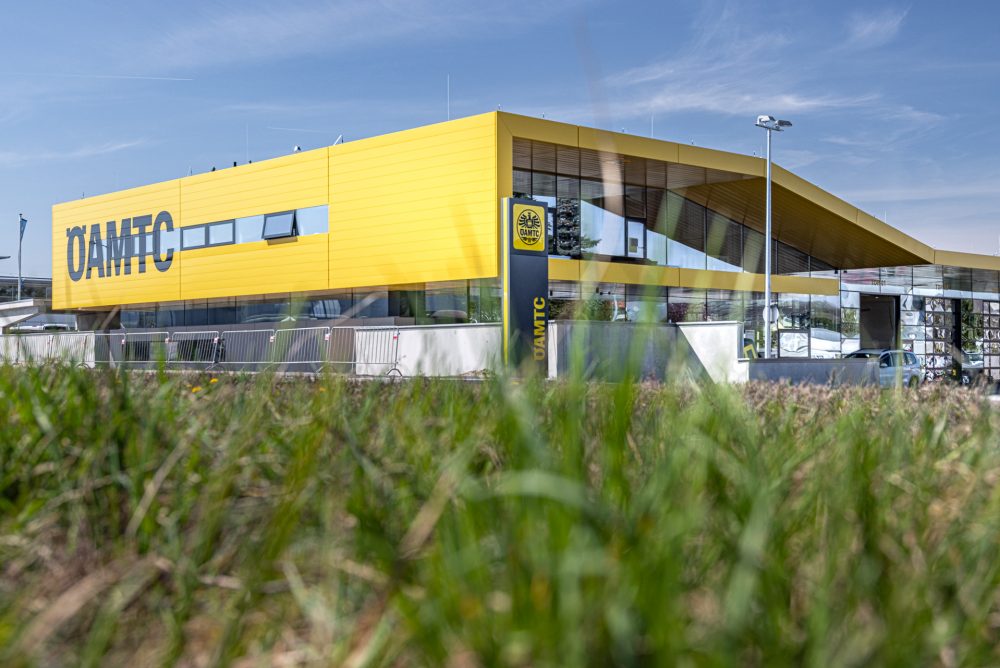 Gelbes Gebäude des ÖAMTC mit großen Glasfenstern, umgeben von Rasen, unter blauem Himmel mit wenigen Wolken.