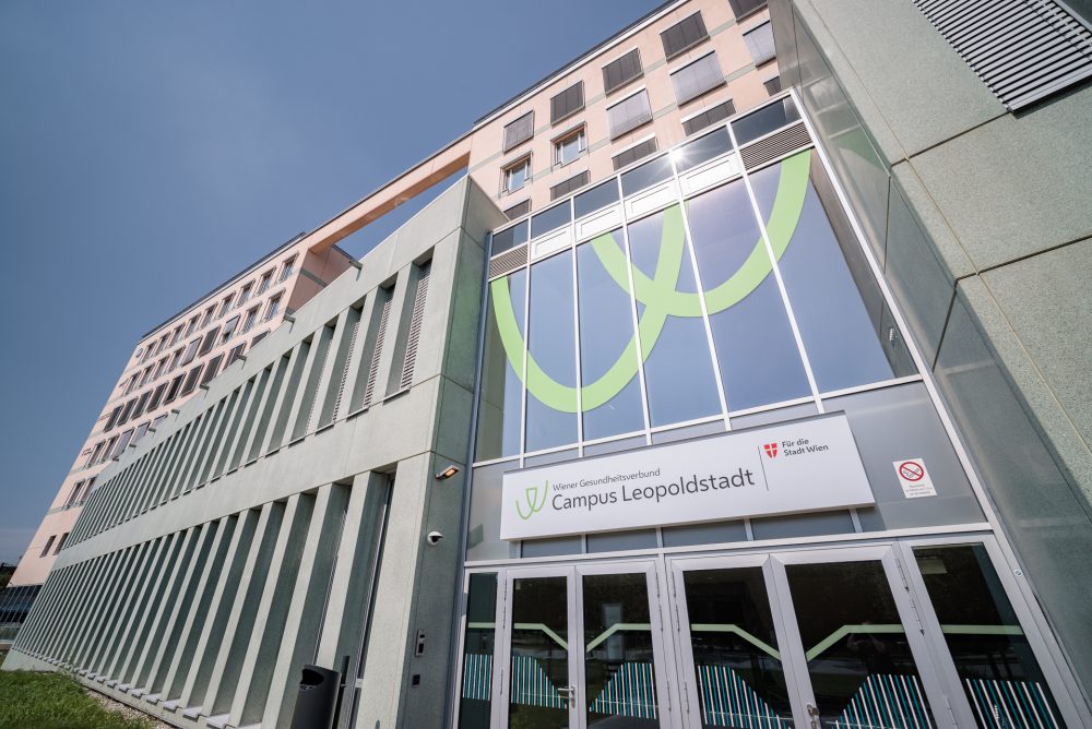 Außenansicht des Campus Leopoldstadt mit modernen Gebäuden, Glasfassade und einem Schild mit dem Logo des Wiener Gesundheitsverbunds.