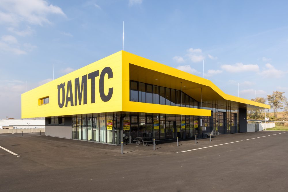 Ein modernes Gebäude mit gelb-schwarzer Fassade und großen Fenstern, auf denen in großen Buchstaben "ÖAMTC" steht.