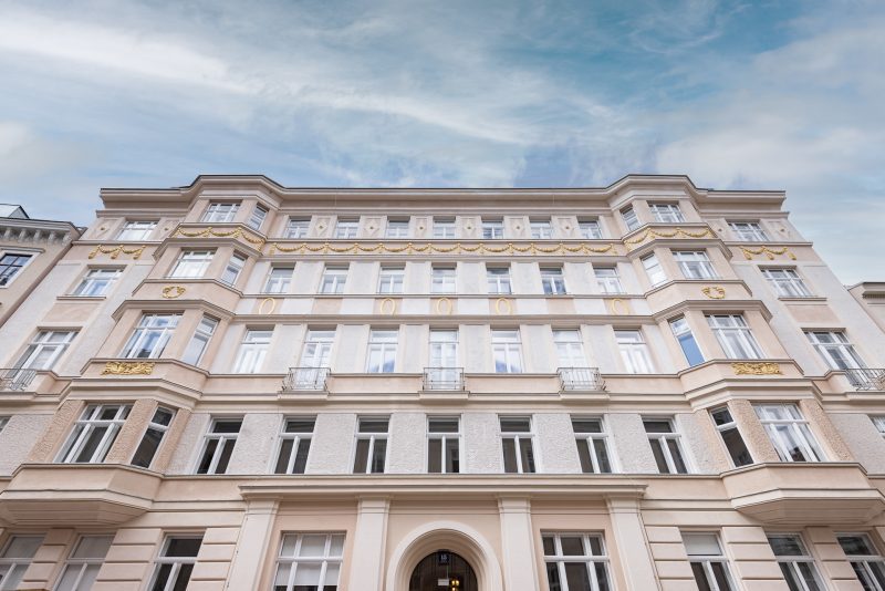 Vorderansicht eines mehrstöckigen, eleganten Altbaus mit verzierten Fassadenelementen und symmetrisch angeordneten, weißen Fenstern.